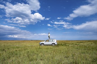 A man stands on a car in the centre of a vast landscape under a blue sky, Yssykköl, Kyrgyzstan,