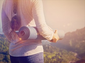 Woman standing with yoga mat outdoors in mountains close up with copyspace. With light leak and