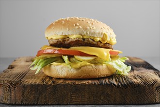 Beef cheeseburger with vegetables and cheesy sauce on wooden board, front view