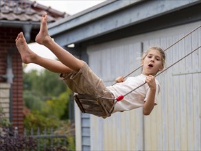 Boy swinging while sitting on children's swing at shed and garden gate, Germany, Europe