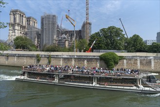 Notre Dame scaffolded, rebuilding after the fire, in front an excursion boat with tourists on the