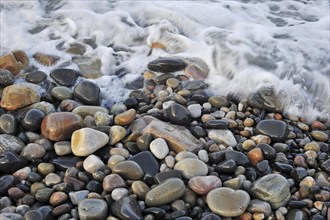 Colourful water smoothed pebbles in surf at shingle beach, Normandy, France, Europe