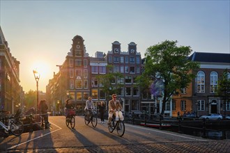 AMSTERDAM, NETHERLANDS, MAY 20, 2018: People on bicycles on Amsterdam bridge over canal with houses