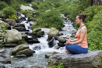 Woman meditating in Hatha yoga asana Padmasana outdoors at tropical waterfall