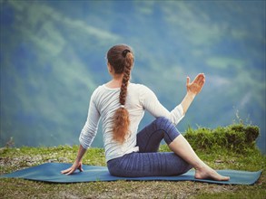 Hatha yoga outdoors, sporty fit woman doing yoga asana Parivrtta Marichyasana (or ardha