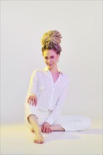 Beautiful young woman in white clothes sits on the floor in light studio