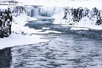 Selfoss waterfall with the river Jökullsa a Fjöllum, icy and snow-covered cliffs and shoreline,