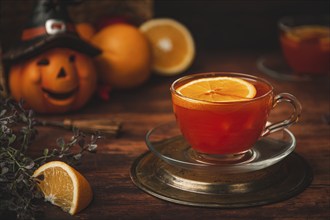 Tea with orange in cup, on wooden background, in front of Halloween decoration