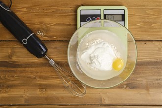 Flour, egg, water and sour cream in a bowl on a kitchen scales, top view