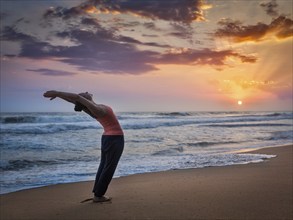 Young sporty fit woman doing yoga Sun salutation Surya Namaskar pose Hasta Uttanasana on tropical