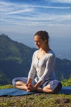 Sporty fit woman practices yoga asana Baddha Konasana, bound angle pose outdoors in HImalayas