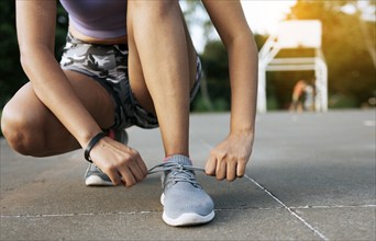 Sport girl tying her shoe laces in a park. Runner girl tying her running shoes in a park with space