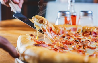 Hand taking a slice of ham pizza with the spatula. Person hand taking a slice of ham and cheese