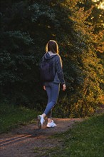 Rear view of a female hiker walks along forest path in rays of sunset