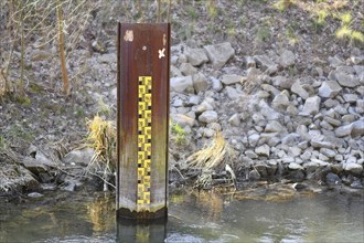 Yellow metric flood level marker in river with low water level