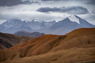 View over red mountainous landscape, high mountains with snow, dramatic dark clouds, Konorchek