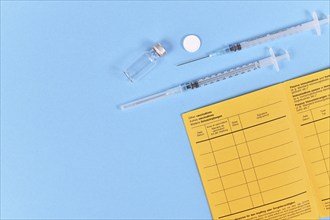 Vaccine concept with syringe, vial and yellow international certificate of vaccination on blue