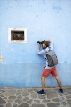 Young man photographed in front of blue house wall, small window with red flower, Burano Island,