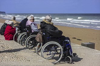 Elderly people in wheelchairs watching the sea on a cold day