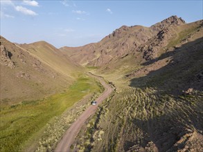 Aerial view, off-road vehicle on gravel road through a mountain valley, Naryn region, Kyrgyzstan,