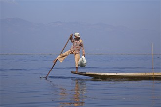 Intha fisherman steering traditional fishing boat by wrapping his leg around the oar, Inle Lake,