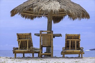 Relaxing bamboo deck chairs with parasol on white sandy beach looking towards ocean at Pantai