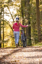 Woman pushing ebike through the autumn forest, Black Forest, Gechingen, Germany, Europe