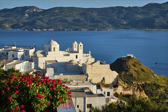 Picturesque scenic view of Greek town Plaka on Milos island over red geranium flowers and Orthodox