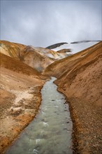 Steaming stream between colourful rhyolite mountains and snowfields, Hveradalir geothermal area,