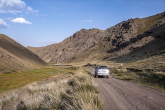 Off-road vehicle at the mountain pass at Songköl, gravel road at a plateau, mountains behind,