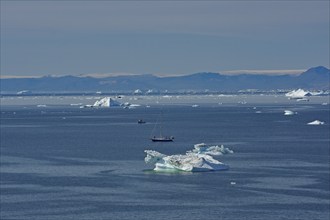 Sailboat in a bay covered with icebergs, Disko Island in the background, Ilulissat, Arctic, Disko