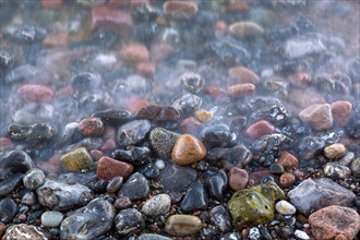 Blurred sea water of wave rolling over wet colourful pebbles on shingle beach, cobble beach