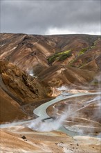 Bridge and steaming streams between colourful rhyolite mountains in the Hveradalir geothermal area,