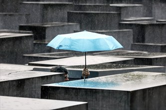 A visitor to the Memorial to the Murdered Jews of Europe protects himself from heavy rain with an