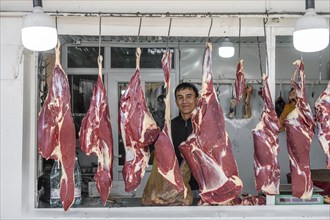 Butcher looking through hung meat, butcher's shop, at the market stall for meat products, Uzgen