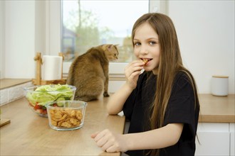 Little nine years old girl bites a cracker while standing in the kitchen