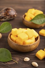 Dried and candied mango cubes in wooden bowls on brown wooden textured background. Side view, close