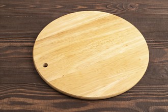 Empty round wooden cutting board on brown wooden background. Side view, close up