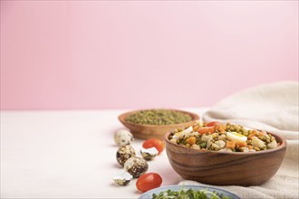 Mung bean porridge with quail eggs, tomatoes and microgreen sprouts on a white and pink background