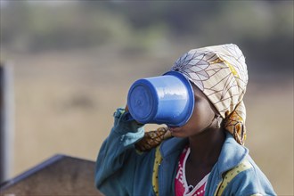 Young woman, girl drinking water from a plastic cup in Maraban Dare community in Plateau state,