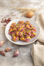 Rainbow colored dumplings with pepper, herbs, microgreen on brown concrete background and linen