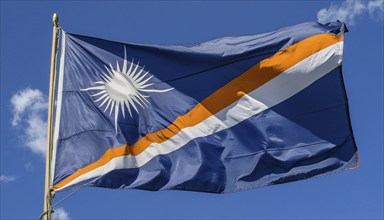 The flag of the Marshall Islands, Pacific Islands, flutters in the wind, isolated against a blue