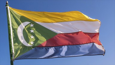 The flag of the Comoros flutters in the wind, isolated against a blue sky