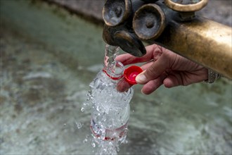 Water fountain, a woman fills drinking water into a small plastic bottle, Munich, Bavaria, Germany,