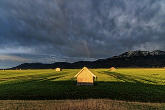 Small wooden hut in a meadow in front of a mountain landscape, storm clouds, thunderstorm, intense