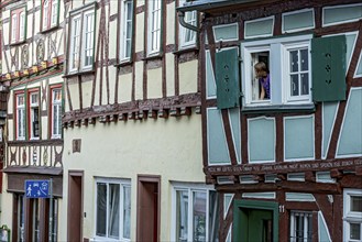 Historic medieval half-timbered houses, row of houses, girl looking out of window onto play street,