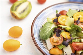 Vegetarian salad of pac choi cabbage, kiwi, tomatoes, kumquat, microgreen sprouts on a white