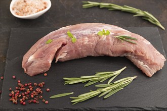 Raw pork meat with herbs and spices on slate cutting board on black concrete background. Side view,