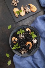 Black cuttlefish ink pasta with shrimps or prawns and small octopuses on black concrete background