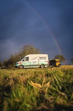 A delivery van drives on a country road with a rainbow in the background, fibreglass construction,